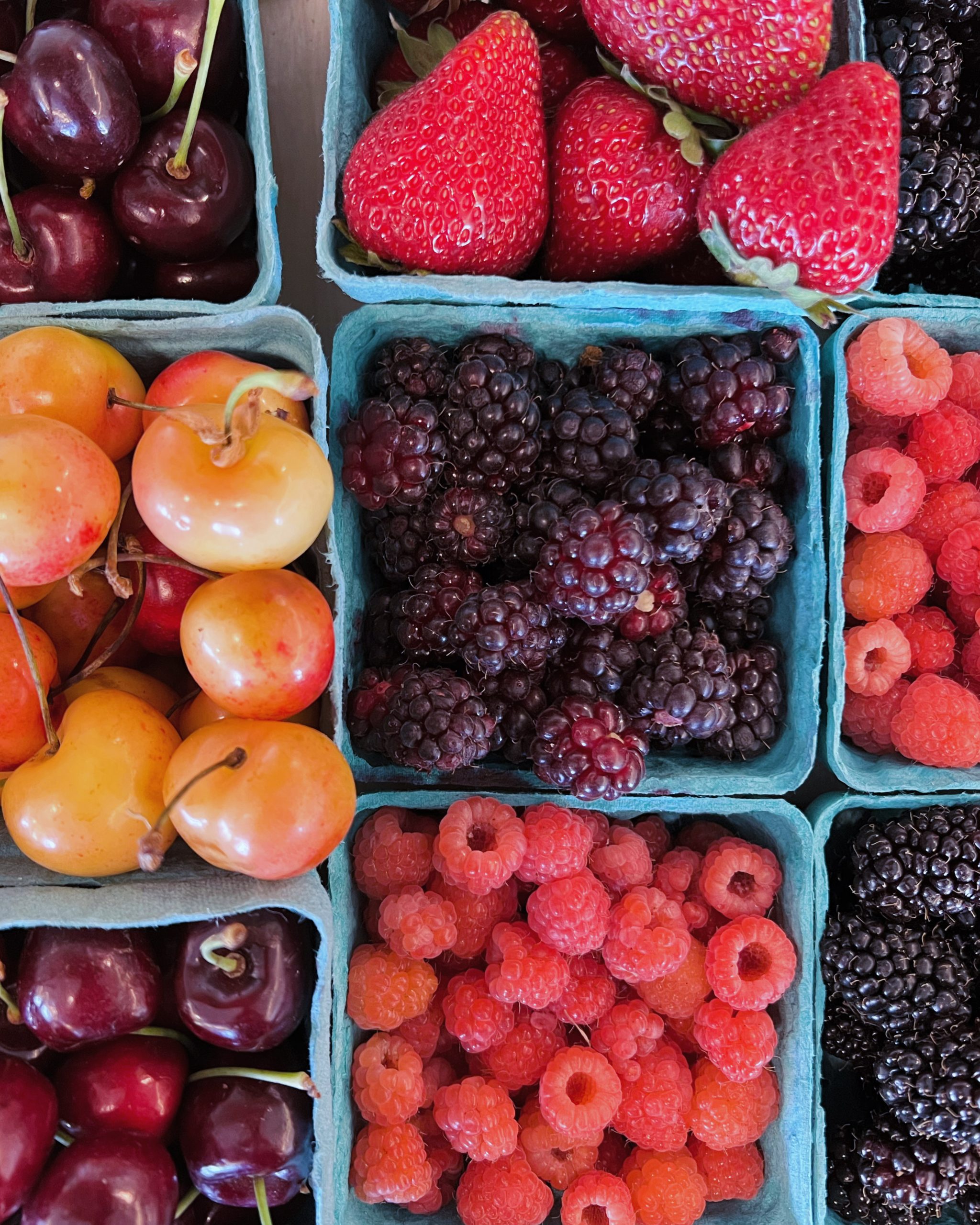 Paper pint containers filled with ripe summer fruit: blackberries, strawberries, raspberries and cherries.