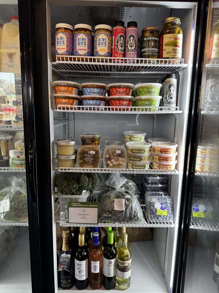A refrigerated case in a neighborhood market features locally-made foods and beverages for sale.