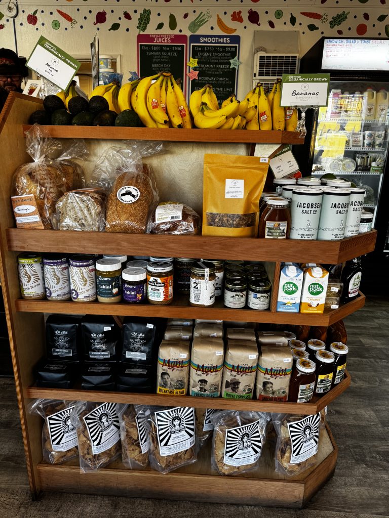 A corner shelf unit in a neighborhood market features produce and grocery items for sale.