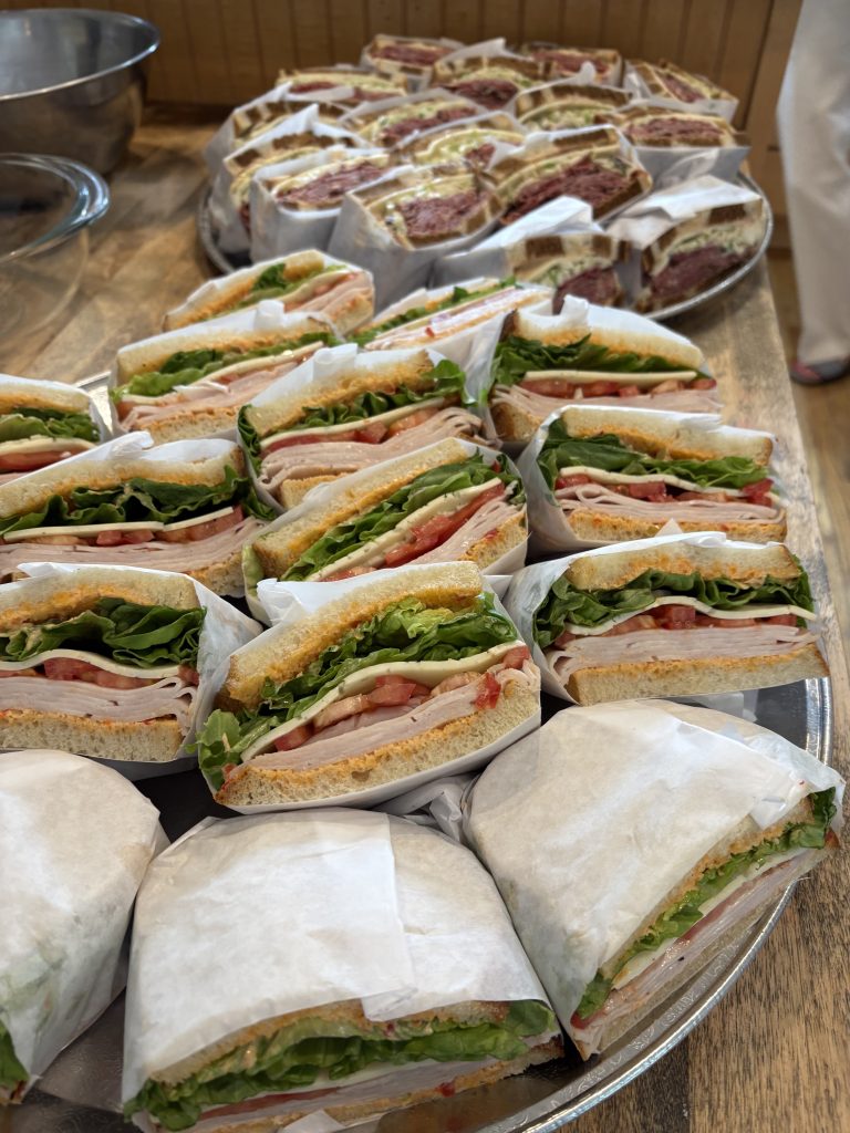 A tray of turkey, cheese, and veggie sandwiches which are cut in half and wrapped in white paper.