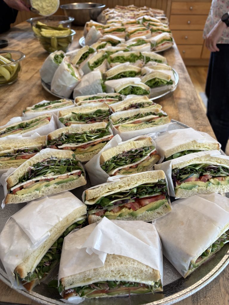 A tray of cheese and veggie sandwiches which are cut in half and wrapped in white paper.