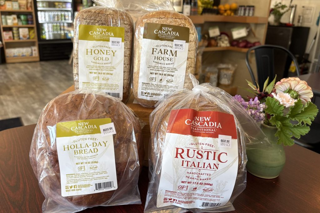 Four loaves of bread arranged on a dark wood table next to a vase of flowers.
