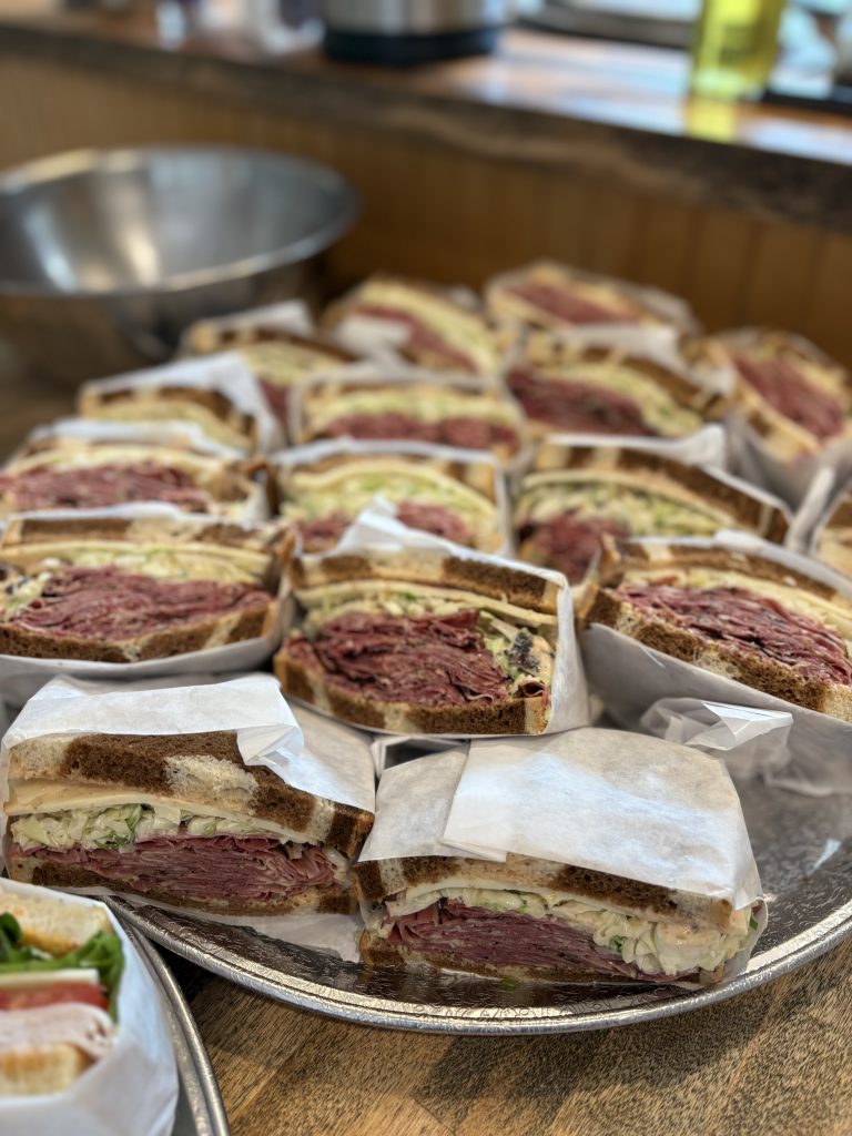 A tray of pastrami sandwiches which are cut in half and wrapped in white paper.