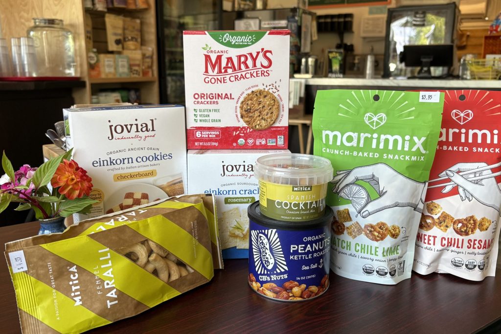 A collection of snack foods is arranged on a dark wood table: crackers, nuts, and packaged cookies.